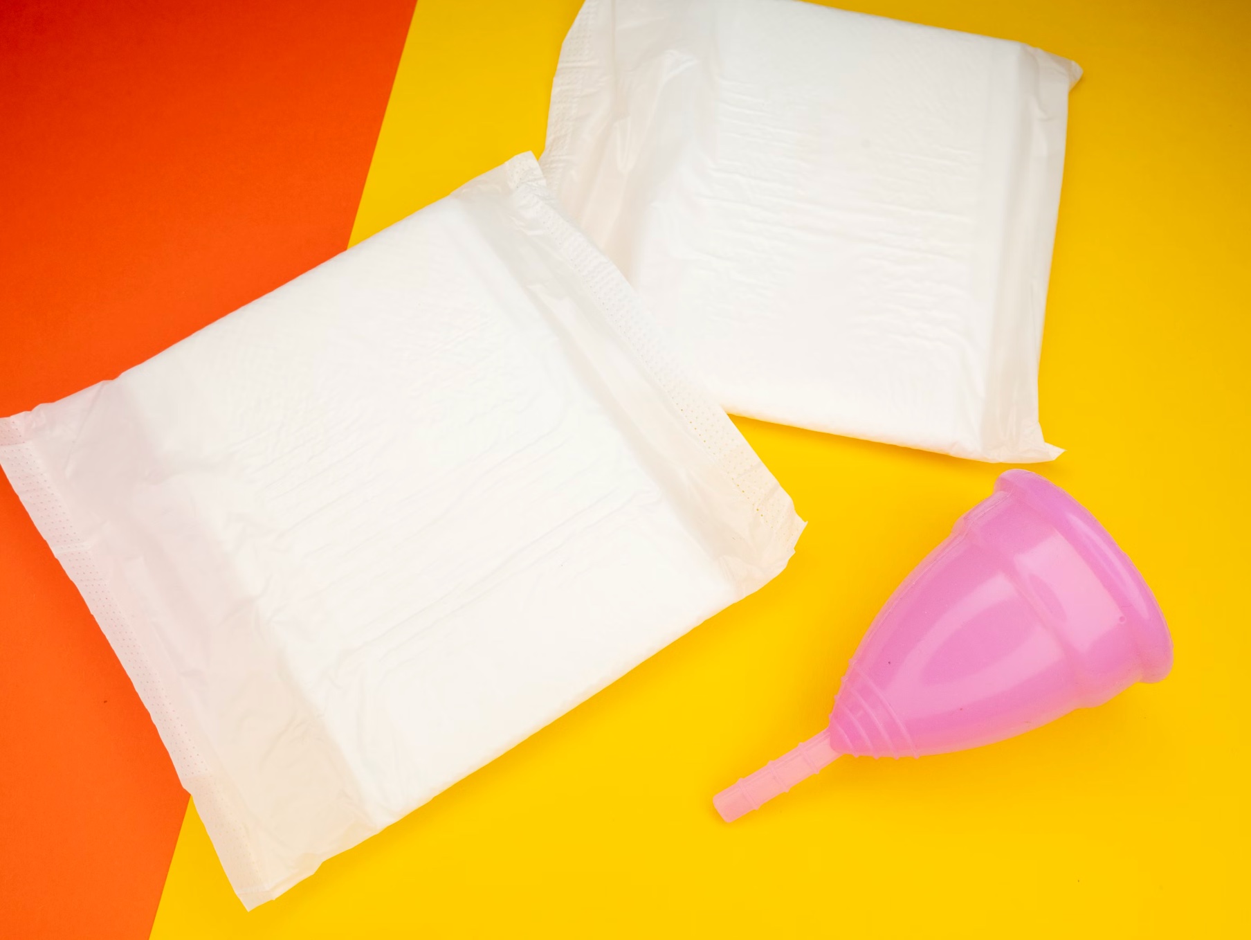 Menstrual cup and sanitary pads on colorful background representing period care